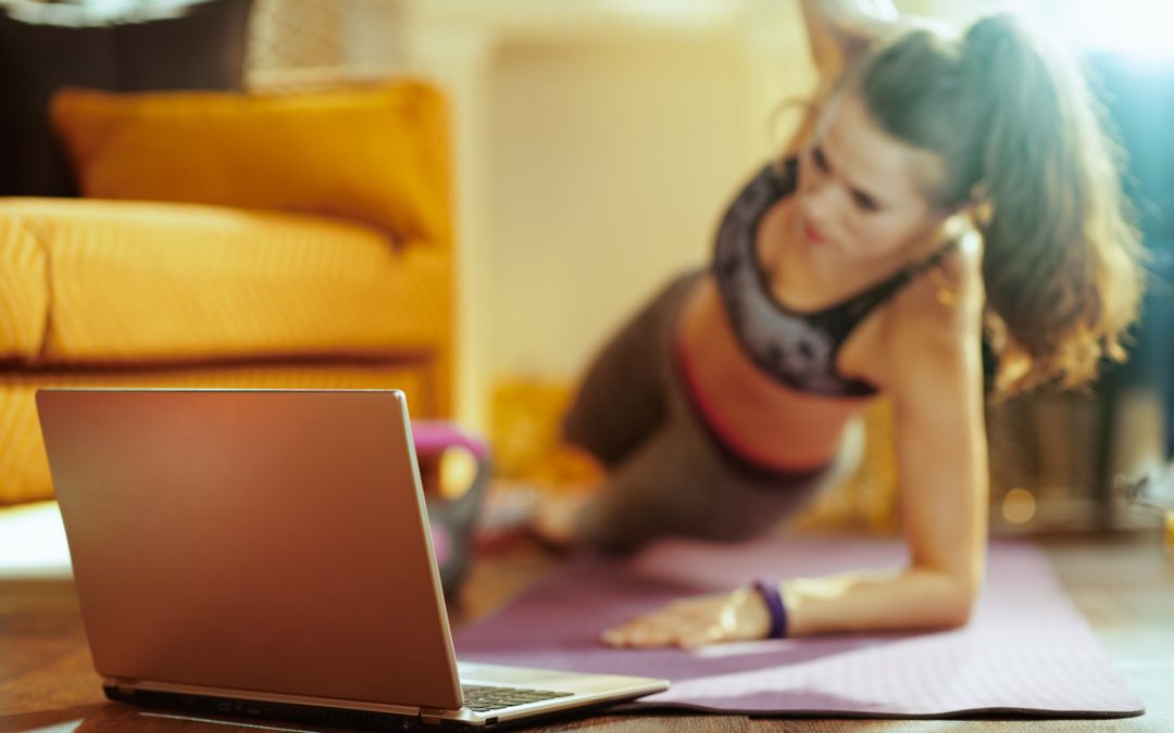 Closeup on laptop and woman in background doing cardio exercises